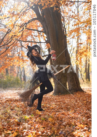 Brunette woman in witch costume standing in autumn forest on Halloween day. Woman wearing black clothes and cone hat. Woman sitting on a broom. Brunette woman in witch costume standing in autumn forest on Halloween day. Woman wearing black clothes and cone hat. Woman sitting on a broom. 105117846