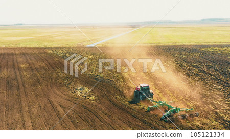 4K Aerial Elevated View.Tractor Plowing Field. Beginning Of Agricultural Spring Season. Cultivator Pulled By A Tractor In Countryside Rural Field Landscape 105121334