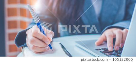 Woman hand is writing on a notepad with a pen and have a laptop computer on the desk in the office. Woman hand is writing on a notepad with a pen and have a laptop computer on the desk in the office. 105122000