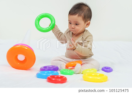 infant baby playing the pyramid toy with colored rings on bed infant baby playing the pyramid toy with colored rings on bed 105125475