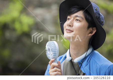 A young man wearing a cool neck ring and using a portable fan at the riverside A young man wearing a cool neck ring and using a portable fan at the riverside 105126110