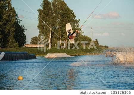 Wake boarding female sportsman girl jumping high wake boarding raley trick with huge water splash in the cable park 105126366
