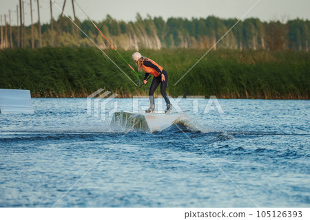 Wake boarding female sportsman girl jumping high wake boarding raley trick with huge water splash in the cable park 105126393