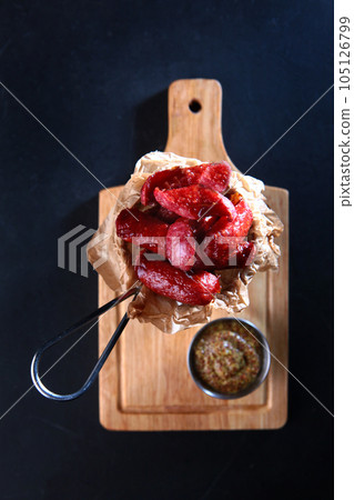 Grilled sausages. A traditional beer snack. Sausages in a metal basket. Mustard sauce. Dijon mustard. Vertical photo on a black background. Flat lay. Top view. 105126799