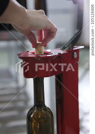 Bottle of wine is corked in production. Natural cork. A small craft winery. The concept of small wine production. Wine of the new harvest. Bottle of wine is corked in production. Natural cork. A small craft winery. The concept of small wine production. Wine of the new harvest. 105126806