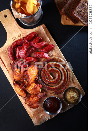 Grilled chicken and smoked sausages on a wooden board. Appetizer for beer. The concept of German cuisine. A set of fried meat and small meat sausages with sauce. Flat lay. Top view. Grilled chicken and smoked sausages on a wooden board. Appetizer for beer. The concept of German cuisine. A set of fried meat and small meat sausages with sauce. Flat lay. Top view. 105126823