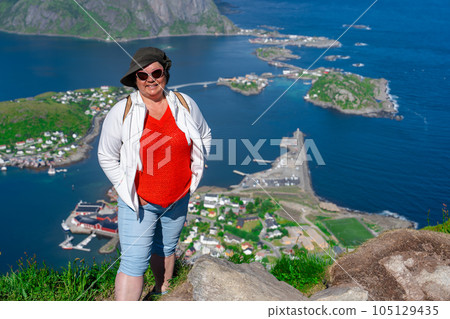Alone happy senior hiker enjoys the view on cliff edge of lofoten islands, in Norway, Reinebringen Alone happy senior hiker enjoys the view on cliff edge of lofoten islands, in Norway, Reinebringen 105129435