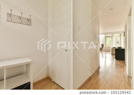a hallway with white walls and wood flooring on the right side, there is an open door that leads to another room 105129542