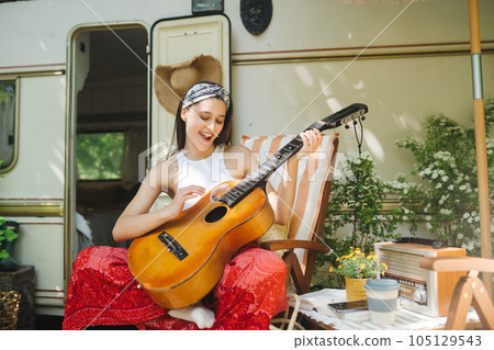 Happy hippie girl is having a good time with playing on guitar in camper trailer. Holiday, vacation, trip concept. 105129543