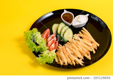 Plate of french fries with lettuce, tomatoes and cucumbers, sauces in white french fries plates. 105129850