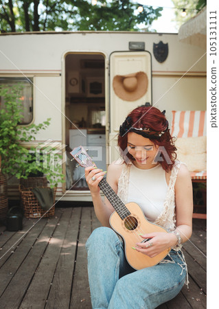 Happy hippie girl is having a good time with playing on guitar in camper trailer. Holiday, vacation, trip concept. 105131111