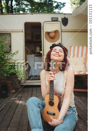 Happy hippie girl is having a good time with playing on guitar in camper trailer. Holiday, vacation, trip concept. 105131115