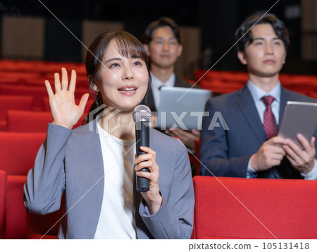 Young woman raising hand to microphone while attending seminar in hall 105131418