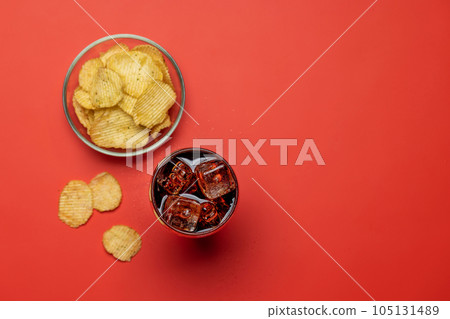 Refreshing glass of cola with ice, accompanied by a serving of crispy chips Refreshing glass of cola with ice, accompanied by a serving of crispy chips 105131489