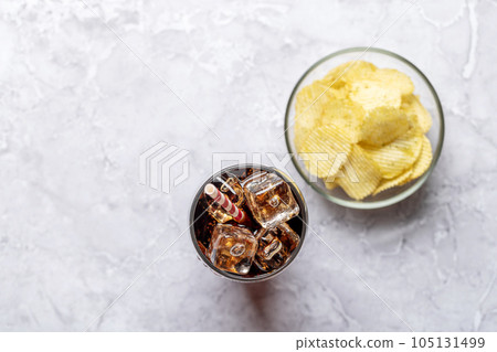 Refreshing glass of cola with ice, accompanied by a serving of crispy chips 105131499