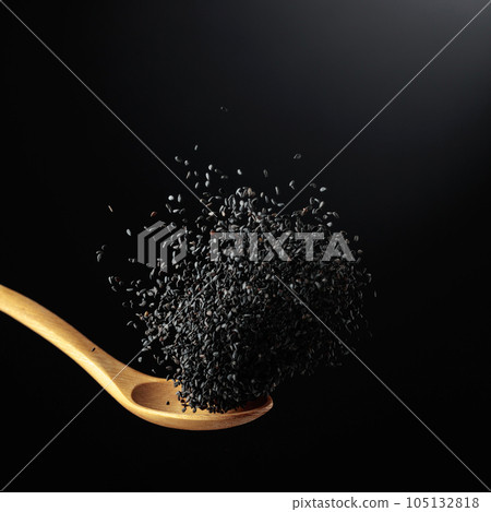 Grains of black sesame is poured with a wooden spoon. 105132818