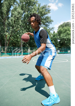 Young man, athlete in blue uniform training, playing basketball outdoors on warm summer day. 105134061