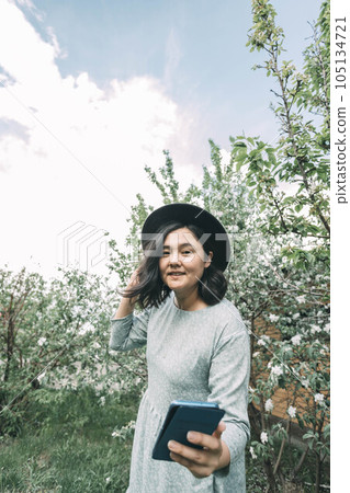 beautiful Asian girl in a hat takes a selfie on a smartphone in a blooming garden beautiful Asian girl in a hat takes a selfie on a smartphone in a blooming garden 105134721