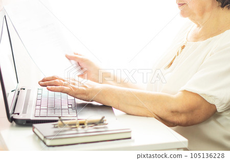 Middle aged senior woman sitting with laptop and paper document, working and tipping on keyboard. Middle aged senior woman sitting with laptop and paper document, working and tipping on keyboard. 105136228