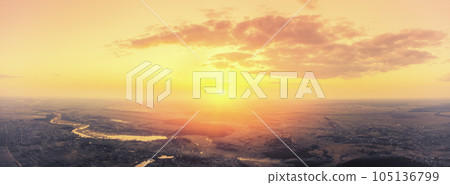 Beautiful sunset in the countryside in spring with the blazing sky. Rural landscape in the evening. Aerial view of brook, village, and arable fields. Panoramic view 105136799