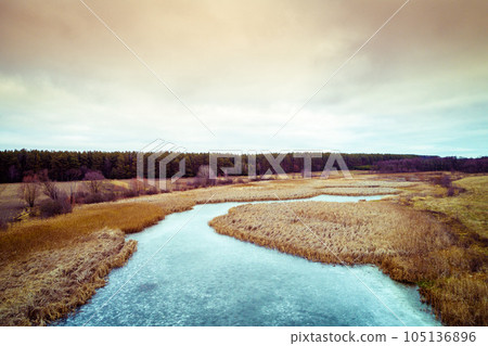 Aerial view of the countryside and frozen winding brook in the evening at sunset light. Beautiful nature landscape with cloudy sky Aerial view of the countryside and frozen winding brook in the evening at sunset light. Beautiful nature landscape with cloudy sky 105136896
