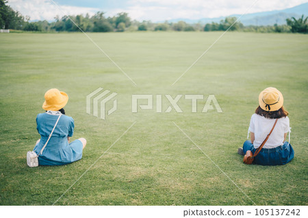 Two women sitting on the grass field, looking to beautiful view and keep space for avoid spreading of virus disease in covid-19 pandemic. Two women sitting on the grass field, looking to beautiful view and keep space for avoid spreading of virus disease in covid-19 pandemic. 105137242