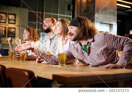 Excited sports fans, friends meeting at pub, drinking beer, watching football match on TV and shouting, cheering up team 105137273
