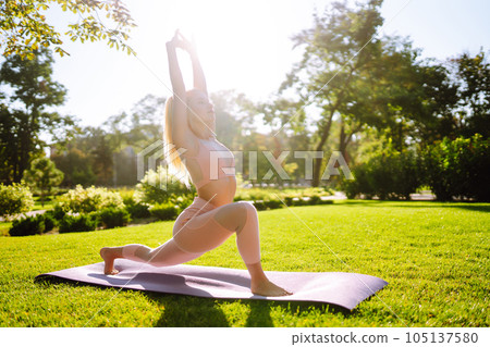 Pretty woman doing yoga exercises in the park. Portrait of woman in sportswear practicing yoga at nature. 105137580