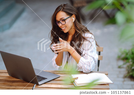 Young woman with wireless headphones calling on laptop, talk by webcam, video conference on cafe. Young woman with wireless headphones calling on laptop, talk by webcam, video conference on cafe. 105137861