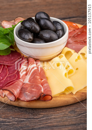 Close-up of a sliced appetizer of sausages, cheese, meat products and olives in a cup. 105137915