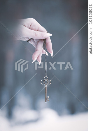 Female pale fingers with sharp nails hold magic silver key in winter forest background, vertical photo, gothic theme, selective focus. Female pale fingers with sharp nails hold magic silver key in winter forest background, vertical photo, gothic theme, selective focus. 105138038