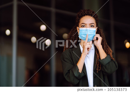 Portrait of a business woman wearing a protective mask with phone solves work issues. Covid-2019. 105138373