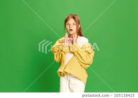 Beautiful little girl looking at camera with shocked face and open mouth over green background. Kids emotions, fashion and beauty concept 105138425