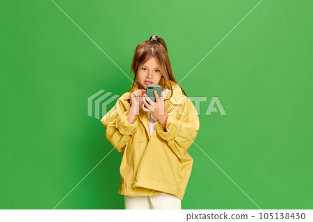 Beautiful little girl looking surprised at smartphone dressed stylishly over green background. 105138430
