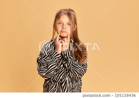 Half-length portrait of charming little girl looking at camera over brown background. Kids emotions, fashion and beauty concept 105138436