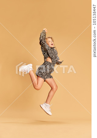Full body photo of beautiful whitehead girl, child in cute animal print suit running smiling on a sandy background 105138447