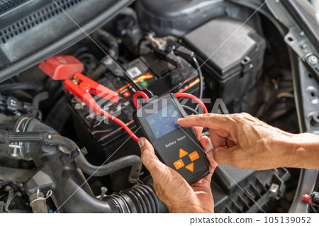 Close up hands of a male mechanic using a battery tester to check on a car battery status 105139052