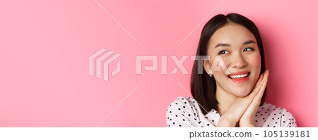Beauty and skin care concept. Headshot of adorable and dreamy asian woman looking left, smiling and imaging, standing against pink background Beauty and skin care concept. Headshot of adorable and dreamy asian woman looking left, smiling and imaging, standing against pink background 105139181