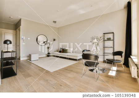 a living room with white walls and wood flooring in the center of the room, there is a large mirror on the wall 105139348