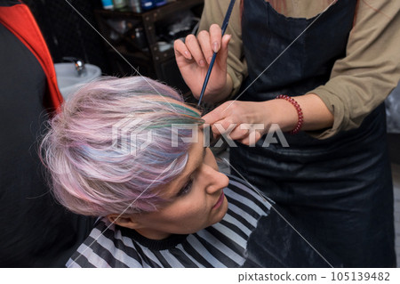 The hands of a girl of an experienced barbershop professional worker in the process of creating a stylish fashionable bob hairstyle creative color coloring 105139482