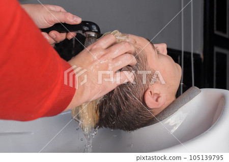The hands of a professional hairdresser wash their hair with rain with water to a client guy over the sink before a haircut 105139795