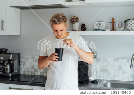 Young man eating a ready dehydrated meal out of portion pot with background of bag with balanced nutritionally complete meals on kitchen table. Food replacement, plant-based protein. Biohacking. 105140460