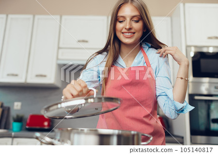 Nice young woman cooking something by the stove in her kitchen Nice young woman cooking something by the stove in her kitchen 105140817