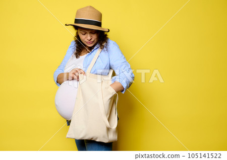 Authentic curly Latina pregnant woman with linen shopper, eco shopping bag on isolated yellow background. Sustainability Authentic curly Latina pregnant woman with linen shopper, eco shopping bag on isolated yellow background. Sustainability 105141522