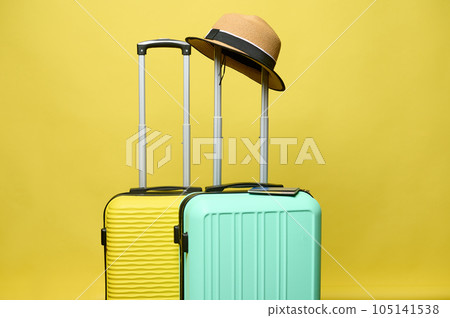 Summer straw hat on the handle of a light green suitcase, isolated over yellow studio background. Travel. Tourism. Trip. Summer straw hat on the handle of a light green suitcase, isolated over yellow studio background. Travel. Tourism. Trip. 105141538