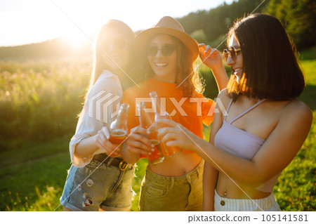 Three woman resting in nature in picnic drinking beer, cheers. Vacation, picnic, friendship concept. Three woman resting in nature in picnic drinking beer, cheers. Vacation, picnic, friendship concept. 105141581