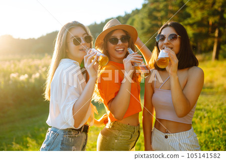 Three woman resting in nature in picnic drinking beer, cheers. Vacation, picnic, friendship concept. Three woman resting in nature in picnic drinking beer, cheers. Vacation, picnic, friendship concept. 105141582