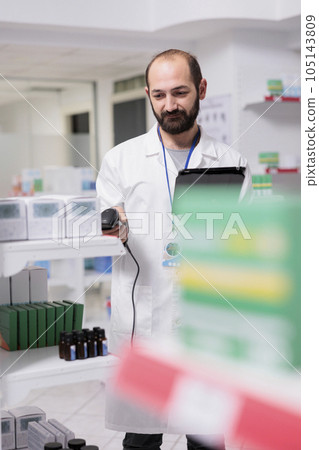 Portrait of pharmacist checking medication list on tablet computer while scanning pills packages using store scanner in pharmacy. Drugstore worker is responsible for organizing and labeling the drugs 105143809