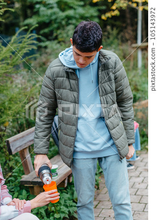 Happy Family drinking tea from a thermos in the forest. Photo of cute charming mother with childrens dressed casual outfit walking sitting bench drinking tea smiling outside city park 105143972