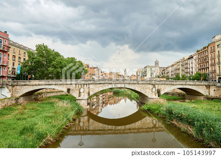 Colorful yellow and orange houses and bridge Pont de Sant Agusti reflected in water river Onyar, in Girona, Catalonia, Spain. Church of Sant Feliu and Saint Mary Cathedral at background. BRIDGE in the Colorful yellow and orange houses and bridge Pont de Sant Agusti reflected in water river Onyar, in Girona, Catalonia, Spain. Church of Sant Feliu and Saint Mary Cathedral at background. BRIDGE in the 105143997